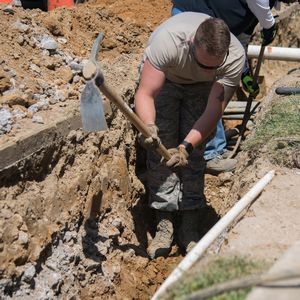 using a mattock to loosen soil in a wide trench